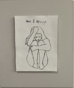 Picture of an Art piece with a girl crouched asking, "am I enough?"