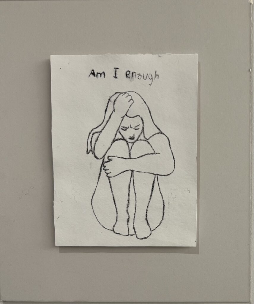 Picture of an Art piece with a girl crouched asking, "am I enough?"